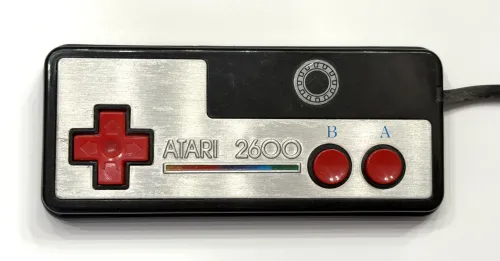 Atari 2600 gamepad with foil metal plate and red D-pad and buttons. Face-on view.