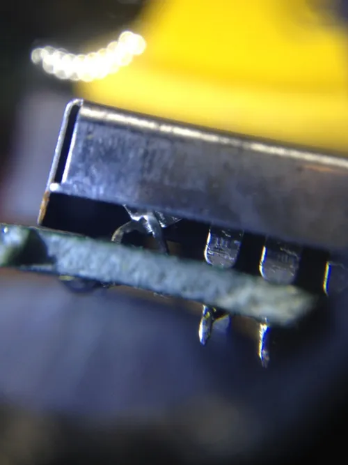 A close-up photo taken edge-on showing two pins coming off of a ROM chip and criss-crossing to effectively create a different pinout to the PCB.